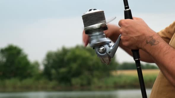 Hands of a Man Holding a Carp Fishing Rod with Reel a Fisherman Catches Fish on the River alt