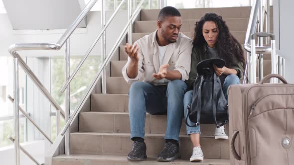 Multinational Couple African Man and Hispanic Woman Sitting at Airport Terminal on Steps with alt