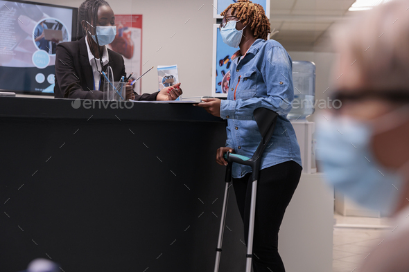 Afro receptionist at health center attending woman on crutches