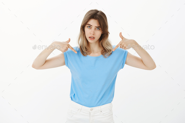 Portrait of unsure insecure attractive woman in blue t-shirt, raising eyebrow with questioned and do