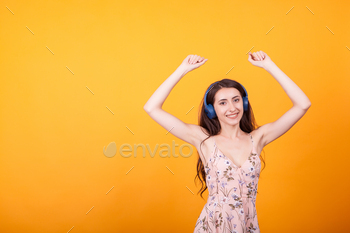 Cute young woman listening music on her headphones in studio over yellow background