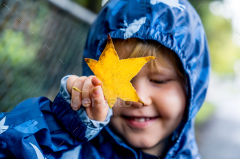 Happy cute caucasian little toddler boy preschooler wearing blue raincoat jacket in the park