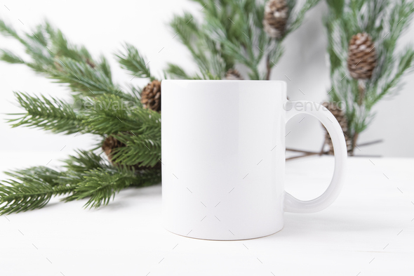 White ceramic cup with space for text or logo on a wooden table with Christmas tree branches
