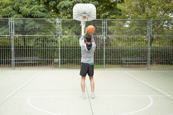 Man throwing a ball from the three-point line on an outdoor basketball court.