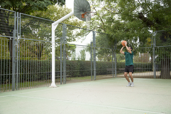 Sportive man throwing a ball from the three-point line on a basketball court