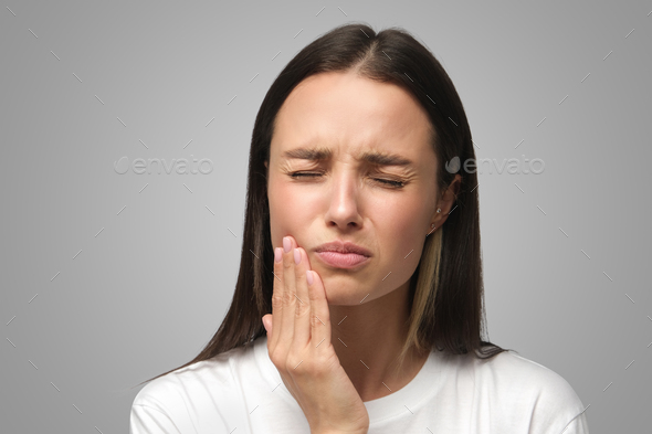 Young female feeling pain, holding her cheek with hand, suffering from tooth ache