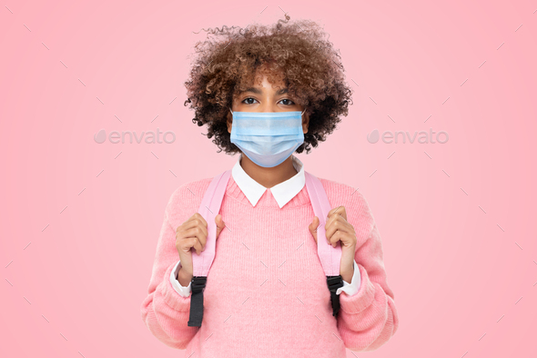 African school girl or college student with afro hair wearing medical mask on pink background