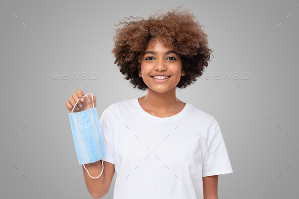 Smiling african girl holding face mask after the end of pandemic, getting back to normal life