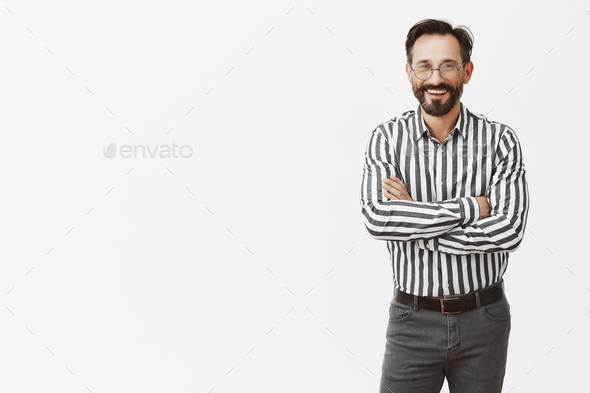 Attractive successful businessman in formal striped shirt and pants, holding hands crossed on chest