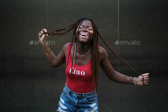 Happy African American woman with vitiligo laughing while holding her hair braids. - Stock Photo - Images