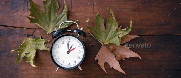 Fall Back, Daylight Saving Time. Yellow clock and autumn leaves on wood