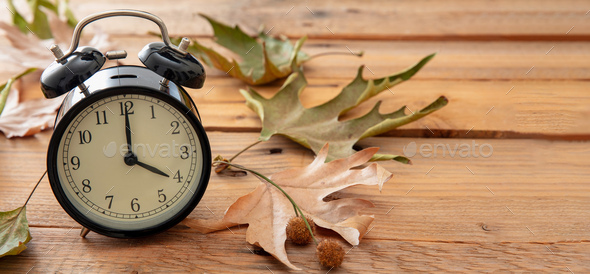 Daylight Saving Time, Fall Back. Black clock and autumn leaves on wood
