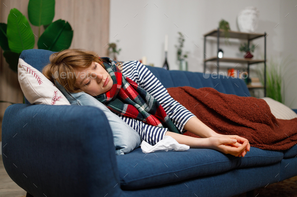 Woman sick with the flu or another virus covered with a blanket sleeps on the couch at home