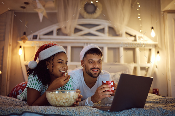 Happy couple watching movie on laptop while spending Christmas Eve at home. - Stock Photo - Images