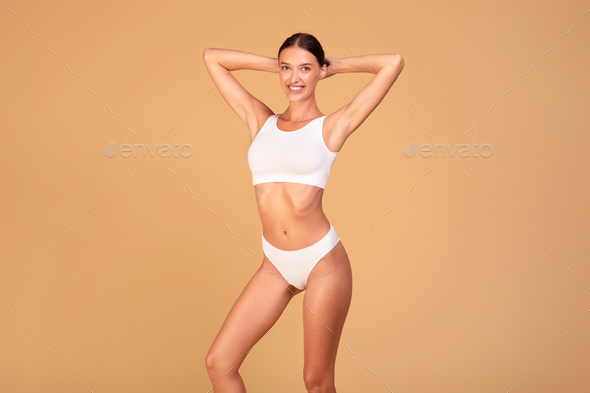 Slim lady with perfect body and flat stomach posing on beige studio background, woman wearing white