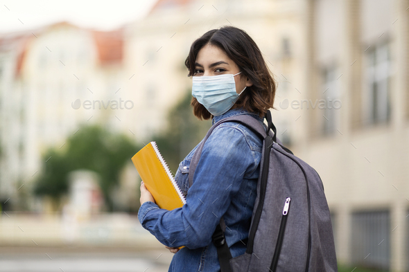 Middle Eastern Female Student Wearing Medical Mask Standing With Workbooks Outdoors