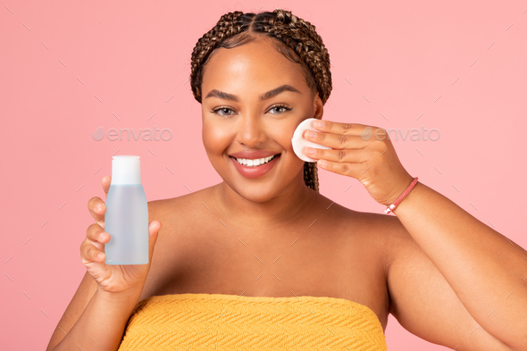 African Lady Using Cotton Pad Holding Cosmetic Bottle, Pink Background