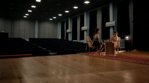 Young boy and girl play a game of chess in a large concert hall