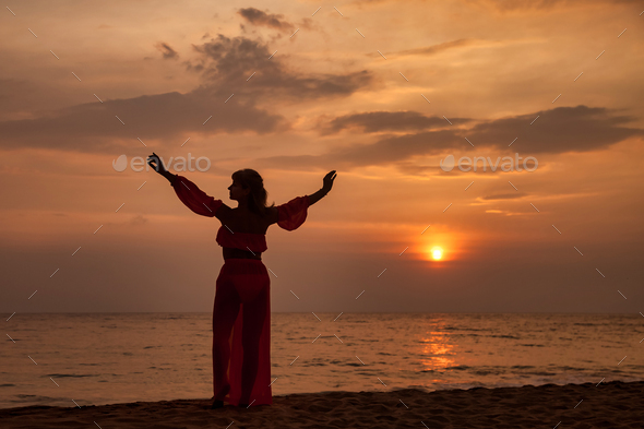 Silhouette middle aged woman arms raised posing on tropical sea sunset. Female relaxing