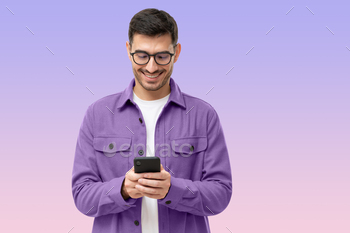 Young man looking at phone, standing on purple background