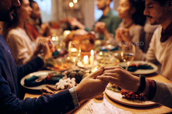Close up of friends holding hands while praying during Thanksgiving meal.