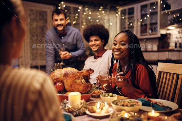 Happy black woman drinking wine and enjoying in conversation with friends during Thanksgiving dinner