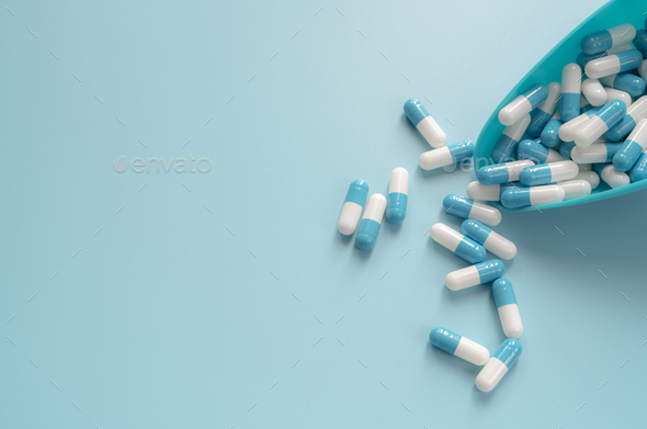 Blue and white capsules pill in plastic spoon and on blue background. Antibiotics drug resistance.