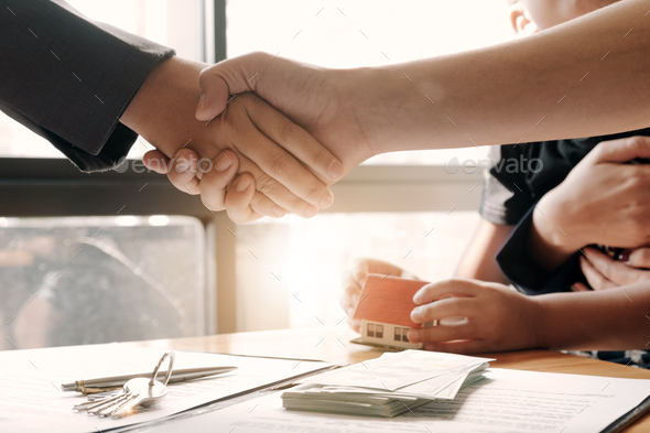 Estate agent shaking hands with his customer after contract signature, Contract document and house
