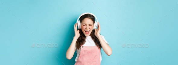 Carefree pretty girl scream from joy, listening music in headphones with happy face, lip-sync