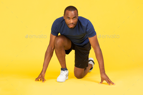 Black Male Runner Standing In Crouch Start Position, Yellow Background