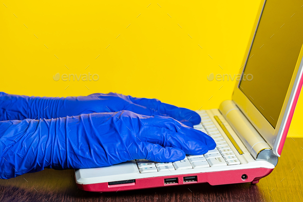 A man in medical latex gloves works at a laptop.