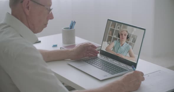 Aged Man Is Watching Online Training Sitting at Home in Front of Laptop, Woman Is Lecturing, Man Is alt