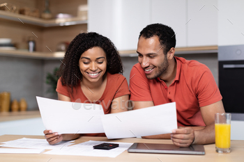 Happy young black couple with tablet pay bills and taxes, work with documents in kitchen interior