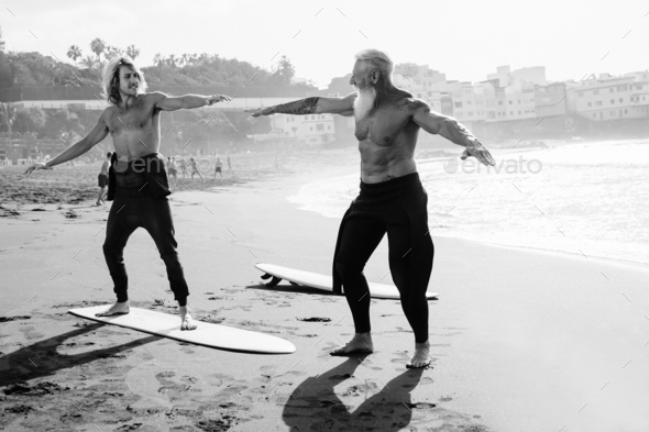 Father and son surfers having fun during surf sport lesson at the beach - Black and white editing