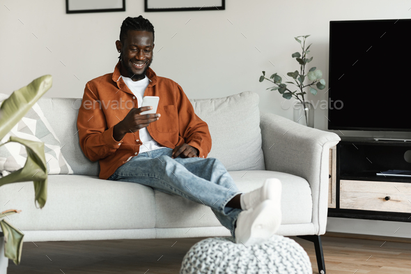 Cool gadget and application. Happy black man holding cellphone, typing sms message, sitting on the