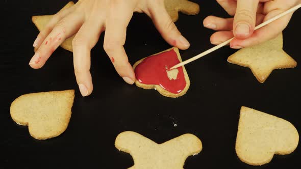 Woman is glazing gingerbread cookie in heart form for St. Valentine's Day alt