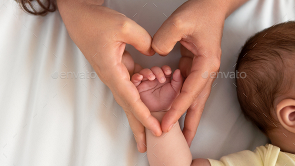 Mom hands holding newborn fingers and giving heart signal love family healthcare