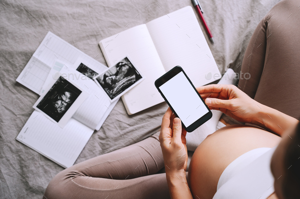 Pregnant woman with smartphone. Closeup pregnant belly with ultrasound photo and medical notes.