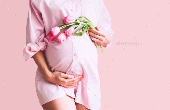 Pregnancy, Motherhood, Mother's Day Holiday concept. Young woman with flowers holds hands on belly