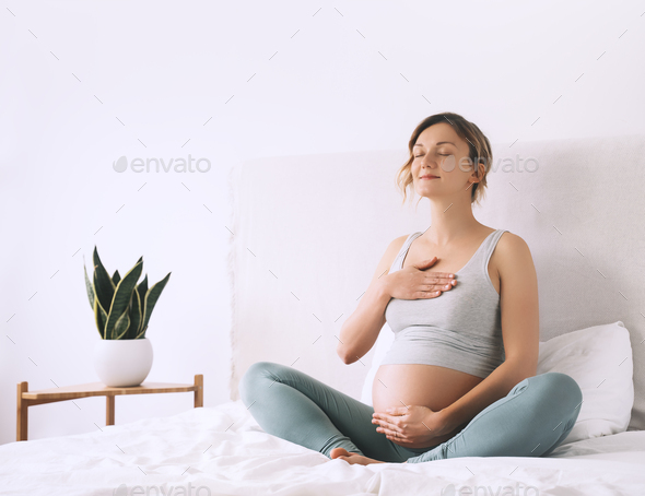 Pregnant woman in lotus pose doing meditation or breathing exercises preparing body for childbirth.