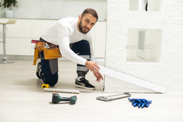 A man installs a floor skirting board. Fixing the plastic skirting board with screws to the wall