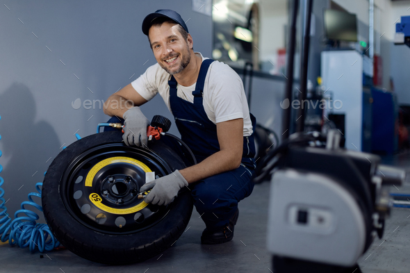 Happy auto repairman checking pressure in a tire while working in repair shop.