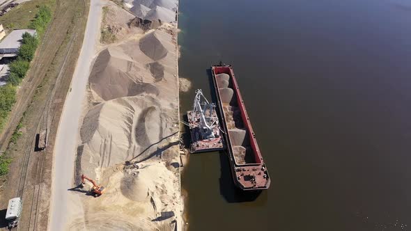 A Port Crane on a River Unloads Sand From a