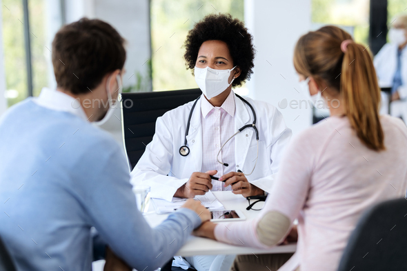African American doctor wearing protective face mask during an appointment with a couple at clinic.
