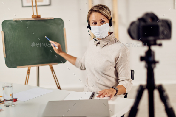 Female teacher with face mask recording video for e-learning during COVID-19 pandemic.