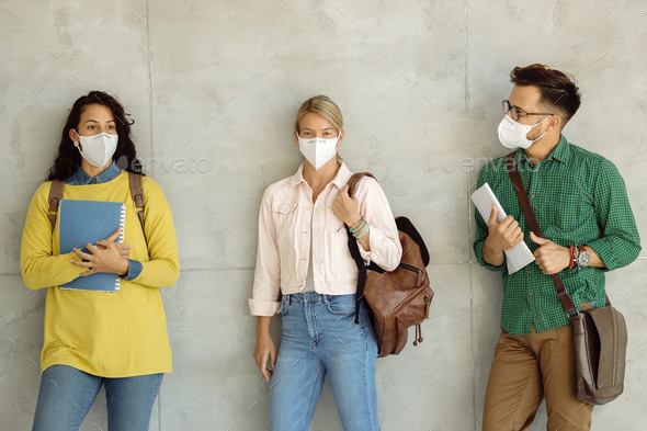 Group of students with face masks standing against the wall at university hallway.