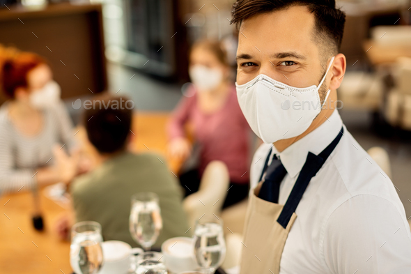 Happy waiter with face mask working in a cafe during coronavirus epidemic.