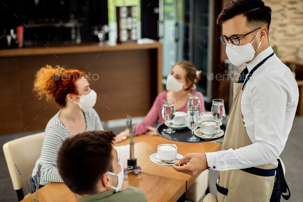 Waiter with face mask while serving coffee to guests in a cafe.
