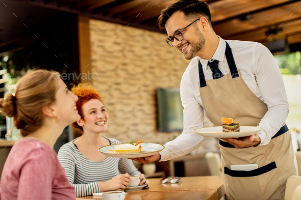 Happy waiter serving dessert to young women in a cafe.