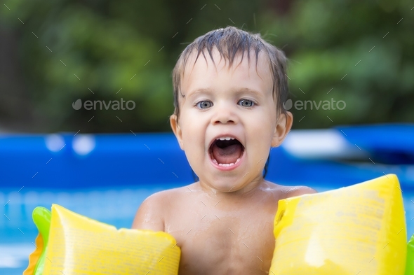 Kid in oversleeves swims in the pool in the yard